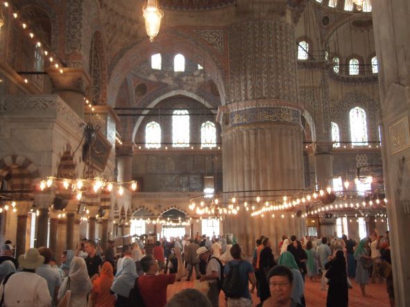 El interior de la Mezquita de Solimán, iluminado para los turistas, con bombillos a media altura, encima de varios turistas tomando fotos